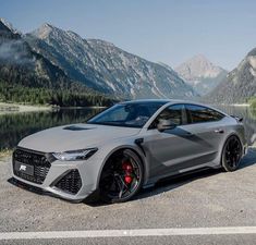 a grey car parked in front of a mountain lake