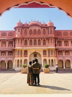 two people standing in front of a large building with arches and pillars on either side