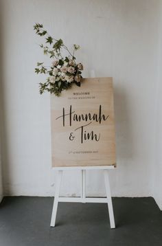 a wooden sign that says hannah and tim with flowers on it in front of a white wall