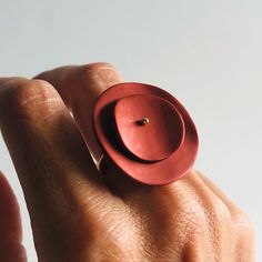 a person's hand holding a red ring with a button on the middle of it