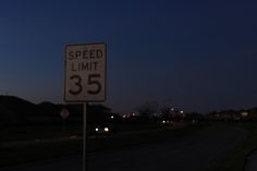 a speed limit sign sitting on the side of a road next to a street at night