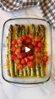 a casserole dish with tomatoes and asparagus in it on a marble table