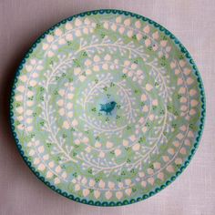 a blue and green plate with white flowers on it, sitting on a tablecloth