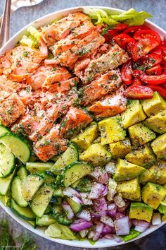 a salad with salmon, avocado, tomatoes and cucumbers in a white bowl