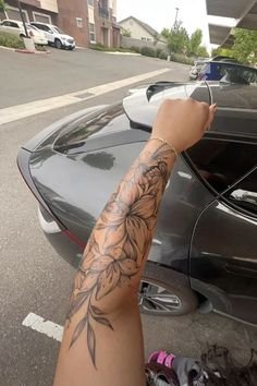 a person with a flower tattoo on their arm next to a parked car in a parking lot