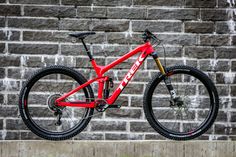 a red mountain bike parked in front of a brick wall