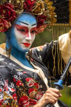 a woman with blue face paint and flowers on her head, holding a black umbrella