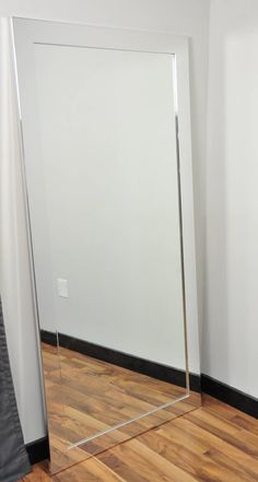 a mirror sitting on top of a hard wood floor next to a white wall in an empty room