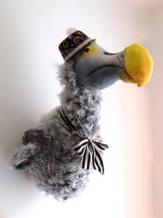 a stuffed bird wearing a crown and holding an apple in its mouth, on top of a white wall