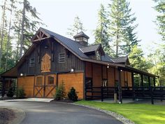 a large wooden barn sitting on top of a lush green field next to a forest