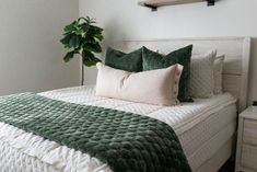 a bed with green and white pillows on top of it next to a potted plant