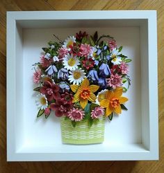 a vase filled with lots of colorful flowers sitting inside of a white frame on top of a wooden floor