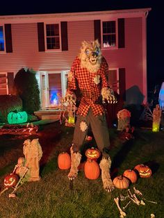 a man dressed as a scarecrow standing in front of a house with pumpkins on the lawn