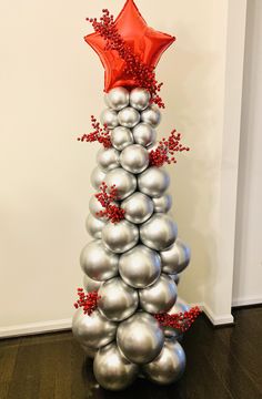 a tall christmas tree made out of silver balls and red star on top, sitting in front of a white wall