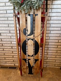 a wooden sled with the word joy written on it and christmas decorations in front of a brick wall