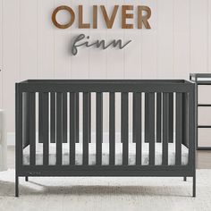 a baby's room with a gray crib and wooden name sign on the wall