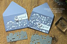 three blue wedding cards with laser cut designs on the front and back, sitting on a wooden table