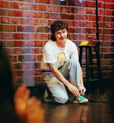 a young man sitting on the floor with his shoes in front of him and a brick wall behind him