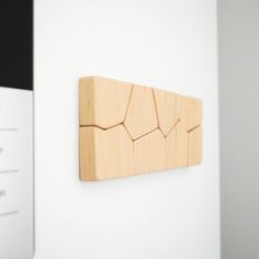 a wooden wall hanging on the side of a white wall next to a black and white cabinet