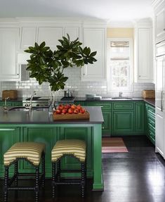 a kitchen with green cabinets and stools in front of the counter top, along with a potted plant on the island