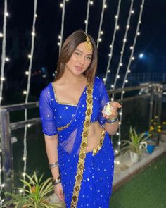 a woman in a blue sari is holding a gold object and posing for the camera