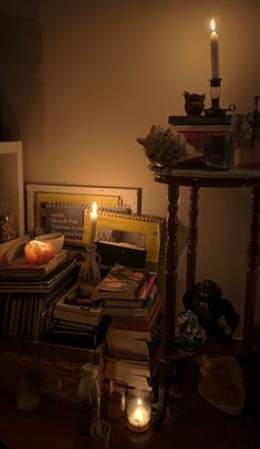 a table topped with lots of books next to a lit candle in a dark room