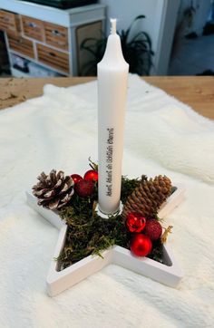 a white candle sitting on top of a star shaped tray filled with pine cones and ornaments