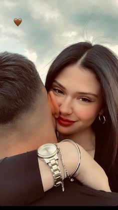 a man kissing a woman's forehead with a watch on her wrist and the sky in the background