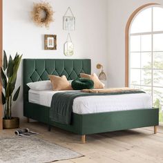 a bed with green headboard and pillows in a white room next to a potted plant