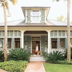 a house with palm trees in front of it and a woman standing on the porch