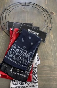 three bandanas hanging from a metal rack on top of a wooden floor next to a pair of scissors