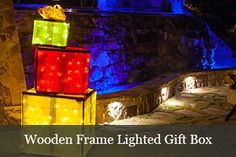 the wooden frame lighted gift box is lit up with colorful lights and sits in front of a stone wall