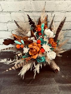 a bridal bouquet with feathers and flowers on a wooden table in front of a brick wall