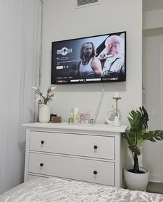 a flat screen tv mounted on the wall above a dresser in a room with white walls