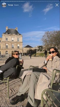 two people sitting on chairs in front of a building with a sky background and one person holding a coffee cup