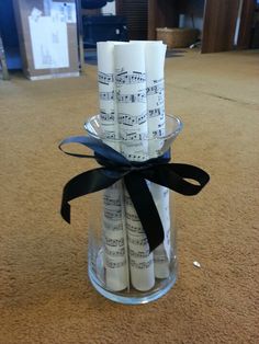 a glass vase filled with white candles covered in sheet music notes and a black ribbon