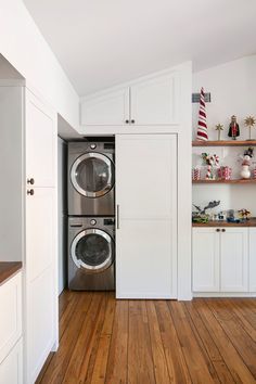 a washer and dryer in a room with white cabinets, wood floors and shelves