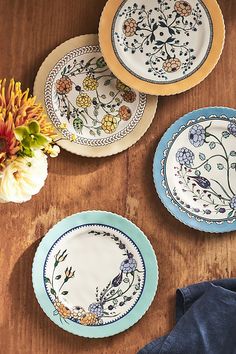 three plates with designs on them sitting on a table next to a flower vase and napkin