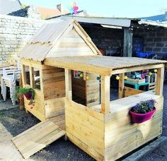 a small wooden house made out of pallet wood with plants in the front yard