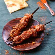 two skewers of meat sitting on top of a wooden plate