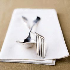 a fork and knife on top of a white napkin next to an empty plate with two forks sticking out of it