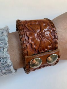 Hand crafted brown leather bracelet with two metal clips with floral design. There is a signature that I can't make out and C9 on the inside - perhaps that's the size. in great condition - measures 1.6 inches high and 2.5 inches in diameter - can be worn on a small or a medium wrist. please look at the pictures as I do not accept returns, thank you for coming to my store Bohemian Brown Flower Jewelry, Vintage Concho Leather Bracelet For Festival, Vintage Leather Concho Bracelet For Festival, Vintage Brown Flower-shaped Jewelry, Vintage Leather Bracelet With Concho, Vintage Hand Tooled Cuff Bracelet For Festivals, Vintage Hand-tooled Cuff Bracelet For Festivals, Brown Bohemian Leather Bracelet With Concho, Handmade Distressed Brown Adjustable Bracelet