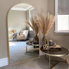 a mirror sitting on top of a table next to a vase filled with dry grass