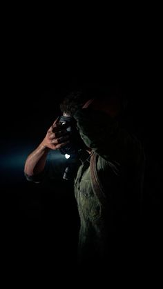 a man holding a camera up to his face in the dark with light coming from behind him