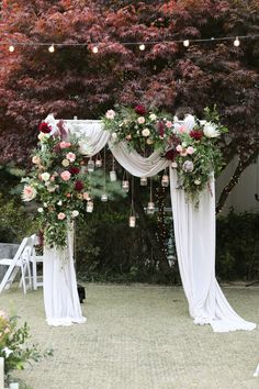 an outdoor wedding setup with white drapes and flowers on the side, surrounded by greenery