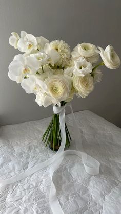 a bouquet of white flowers in a glass vase on a lace tablecloth with a ribbon