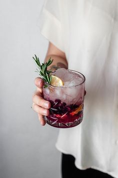 a woman holding a glass with a lemon and rosemary garnish