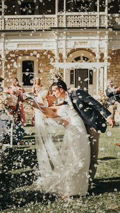 a bride and groom standing under an umbrella in front of their wedding guests at the end of confetti throwing