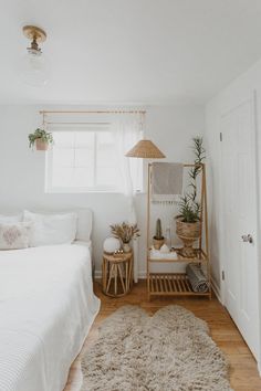 a bedroom with white walls and wooden flooring is pictured in this image, there are plants on the nightstands next to the bed