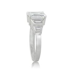 A beautiful Estate Emerald Cut Diamond Engagement Ring, accented by a tapered baguette and bullet-cut diamonds on either side. Modern Emerald Ring With Gia Certified Diamond, Modern Gia Certified Emerald Ring With Diamond, Modern Gia Certified Emerald And Diamond Ring, Modern Gia Certified Emerald Cut Diamond Ring, Timeless Three Stone Emerald Ring For Formal Occasions, Platinum Emerald Cut Ring With Bezel Setting, Modern Emerald Cut Lab Grown Diamond Ring, Modern Emerald Ring With Vvs Clarity And Baguette Cut, Diamond White Three-stone Emerald Cut Jewelry